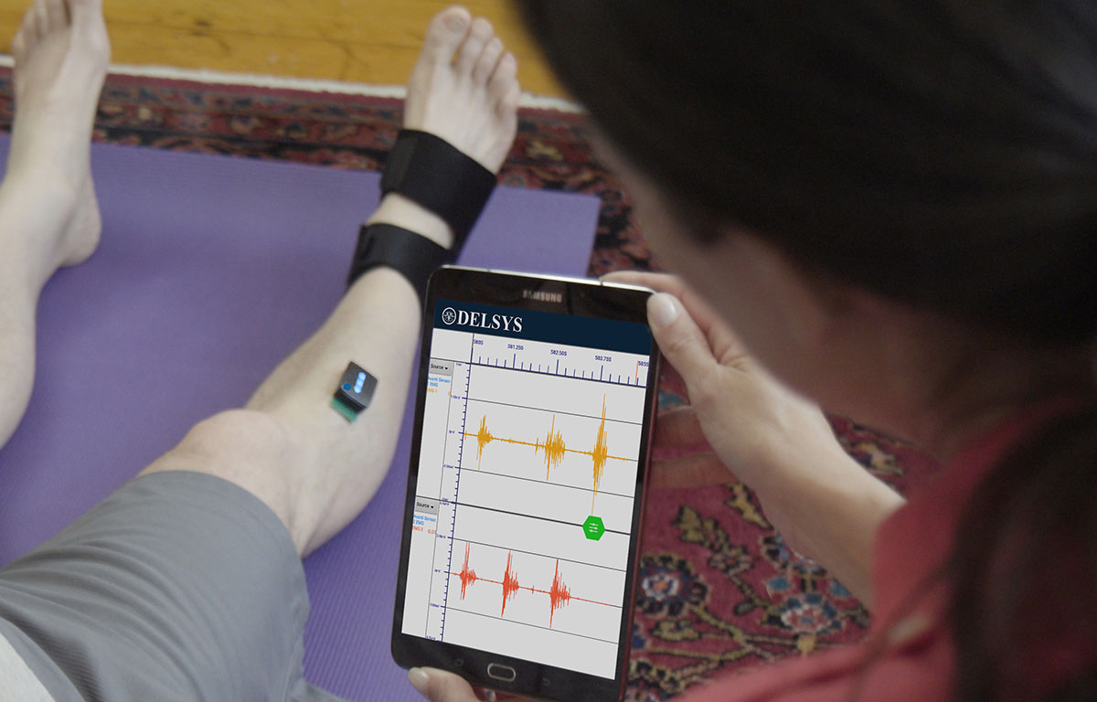 Elderly man wearing Trigno Avanti sensor on legs. Woman holding onto a tablet loaded with Mobile EMG Suite