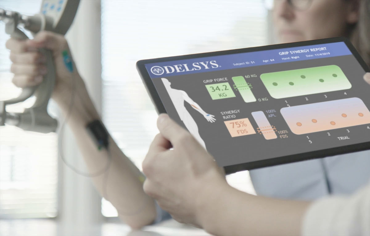 Woman with Trigno Duo sensor on arm, holding onto a JAMAR dynamometer. Man holding onto a tablet loaded with EMG Grip Android app.